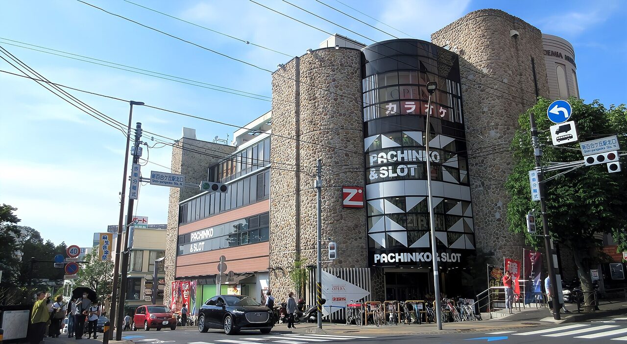 新百合ヶ丘駅の北口の交差点。石積みの壁の建物の前に横断歩道があり、右の柱に「新百合ヶ丘駅北口」の案内標識が見える