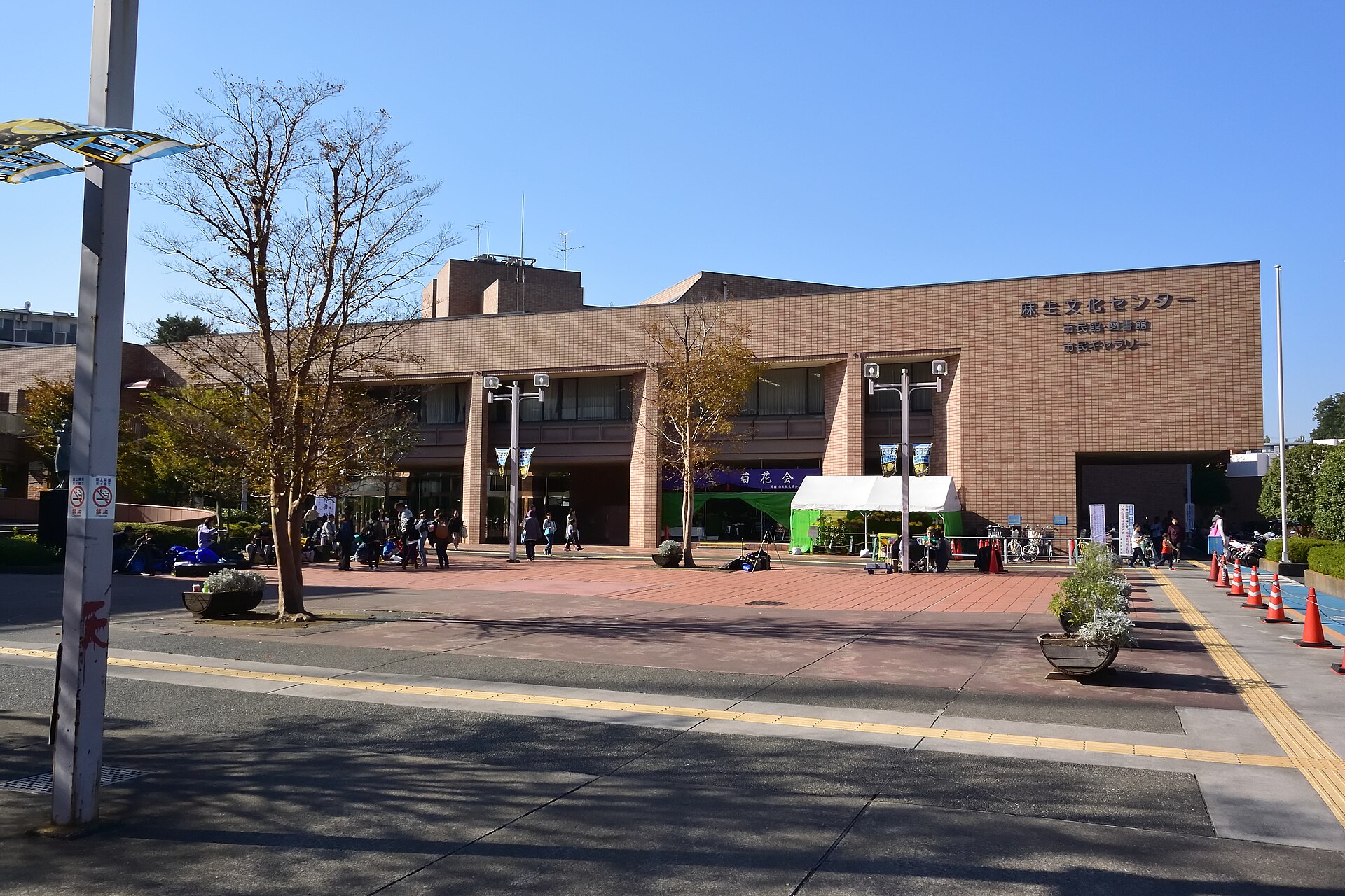 れんが色の外壁に「麻生文化センター　市民館・図書館　市民ギャラリー」の文字が見える建物。手前に広場がある