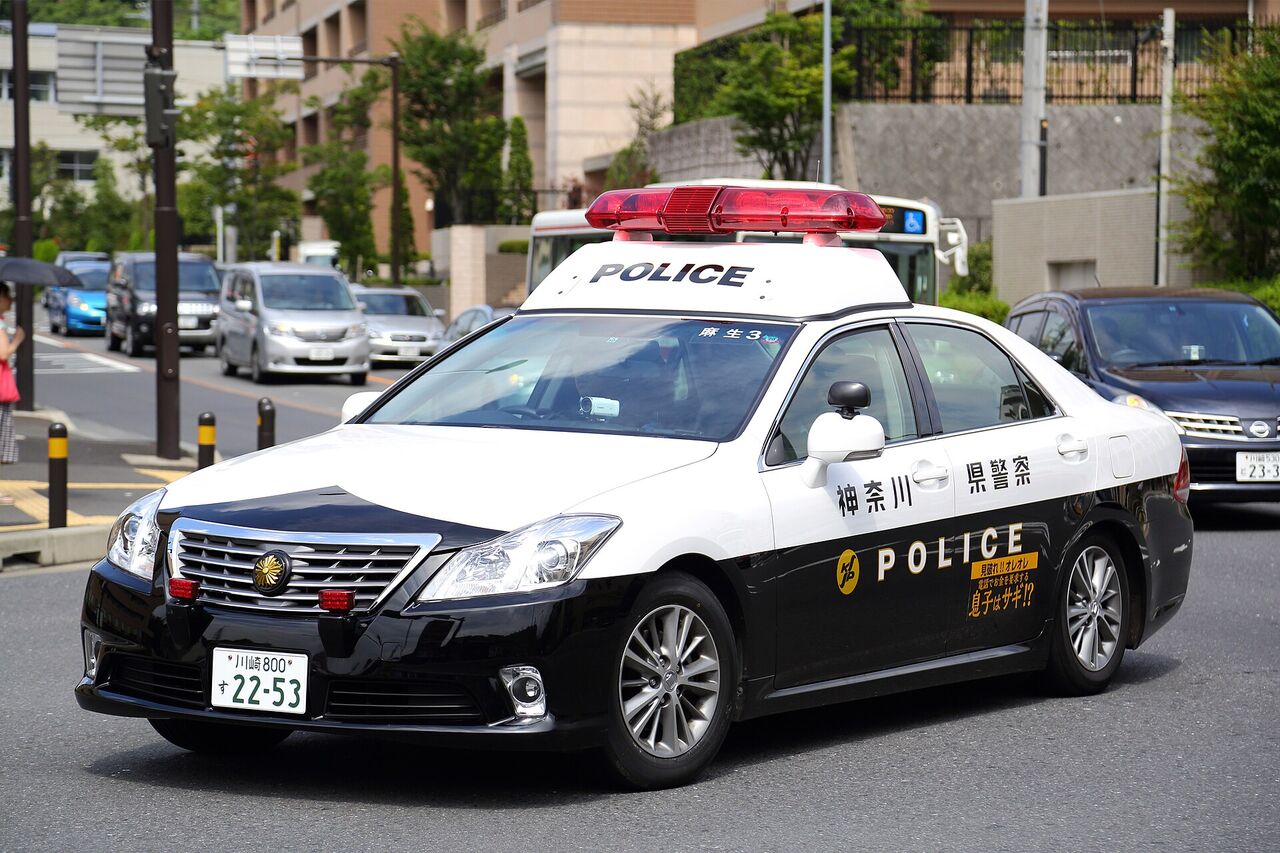 交差点を走る、白と黒のパトカー。ドアに「神奈川県警察」と書かれ、後ろのドアには、オレオレ詐欺への注意を呼びかけるステッカーが貼られている
