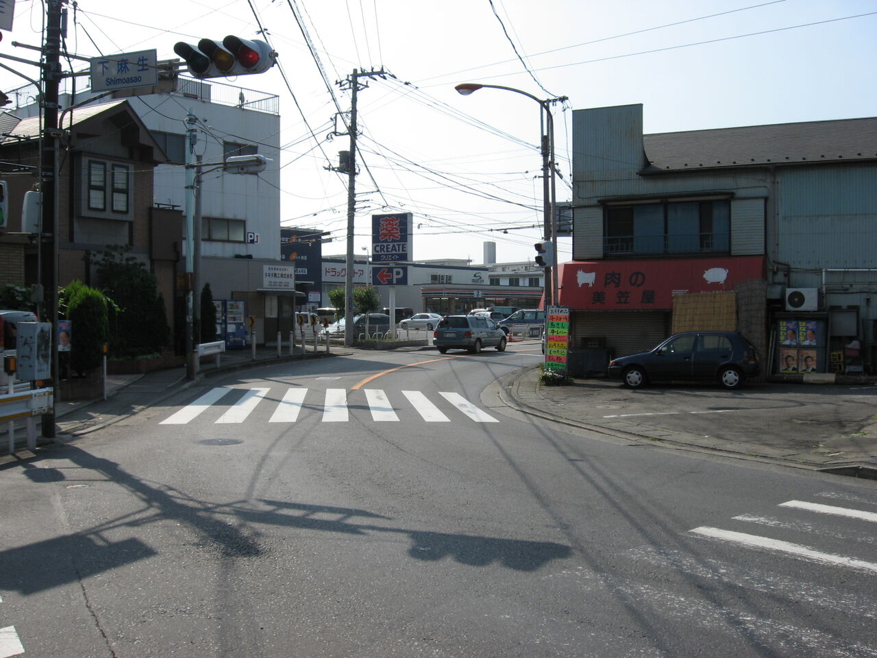 下麻生交差点。信号機のある交差点に横断歩道があり、両側に住宅と店が並ぶ