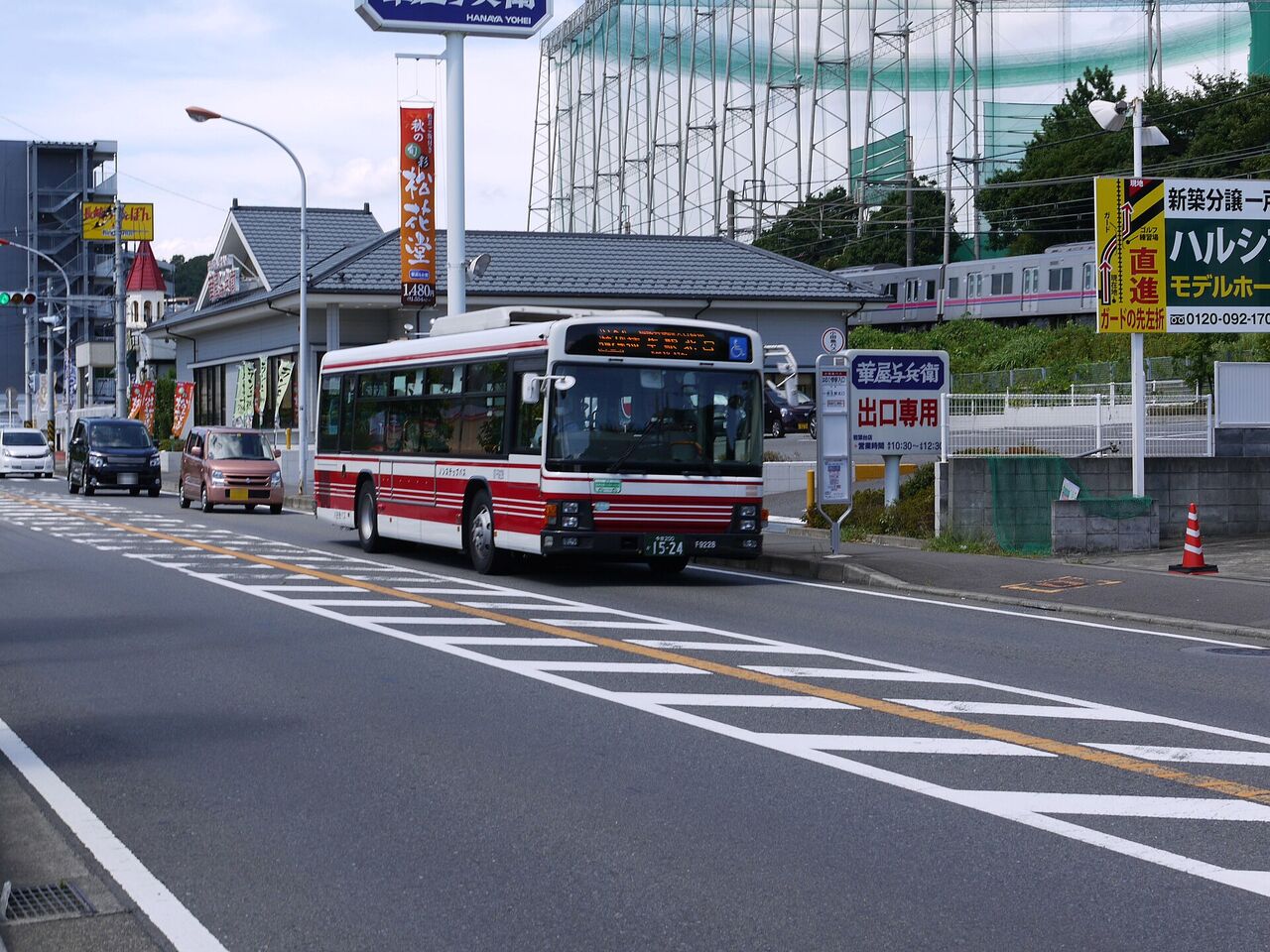 はるひ野駅入口のバス停の前を走る、小田急バス。道路の奥に看板と建物が見える