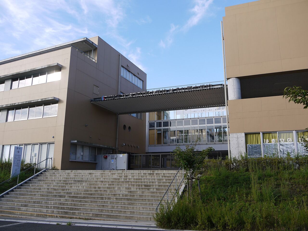 はるひ野小学校・はるひ野中学校の入口。大きな階段の上に、二つの校舎をつなぐ通路と、学校名の看板がある