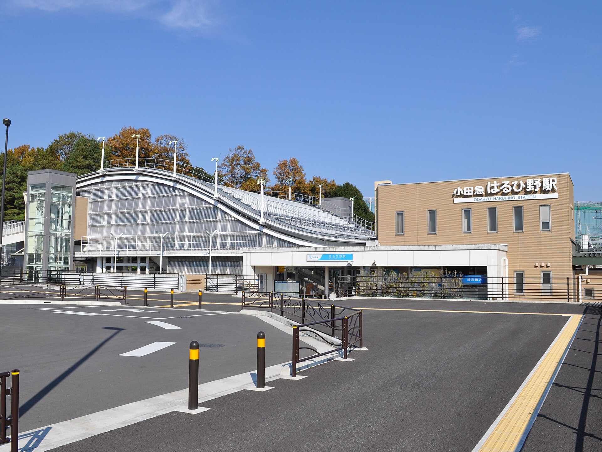 はるひ野駅の外観。波のような屋根の駅舎と、「小田急 はるひ野駅」の看板がある建物。奥に木々が見える