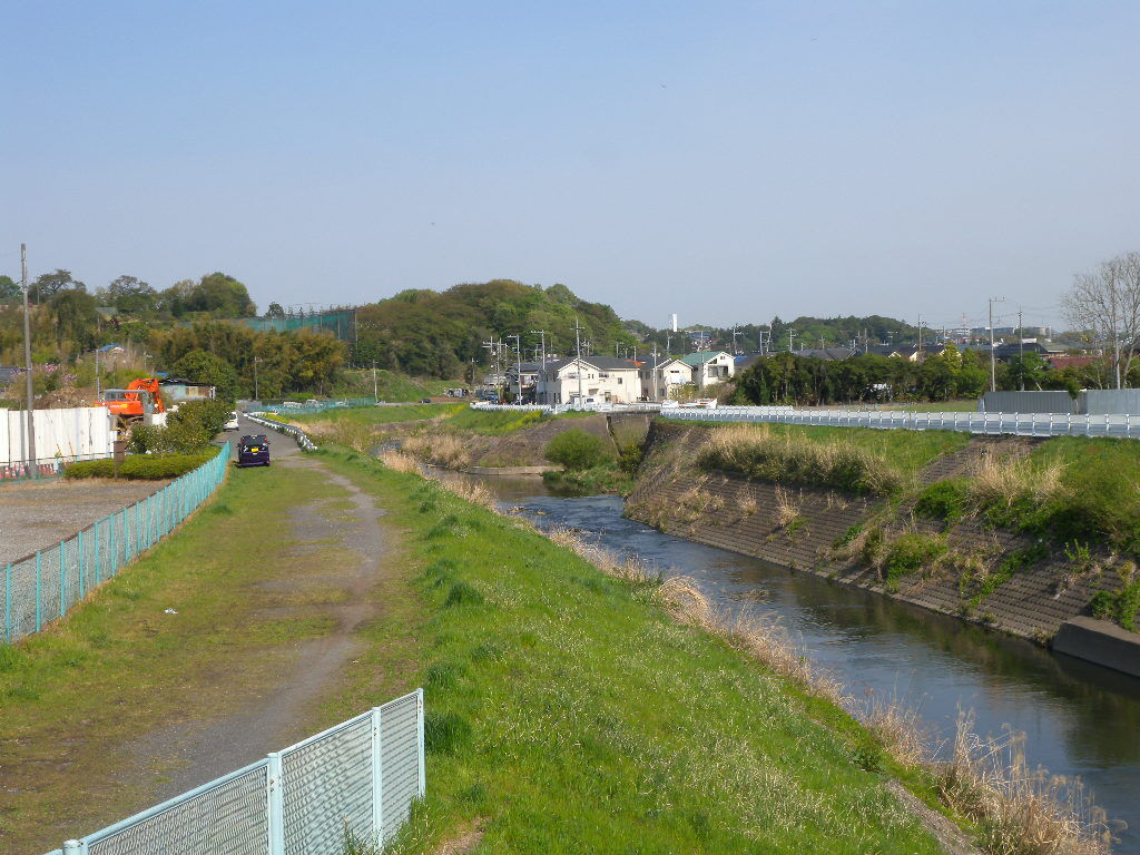寺家橋から見た鶴見川と早野川の合流点。川沿いに草の土手と道が続き、奥に住宅と緑の丘が見える