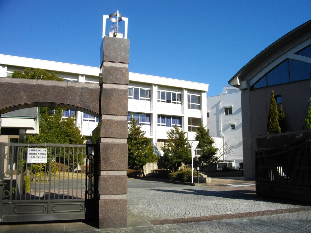 東百合丘にある田園調布学園大学の門。石の門柱の奥に、白い校舎と木々が見える（2012年1月撮影）