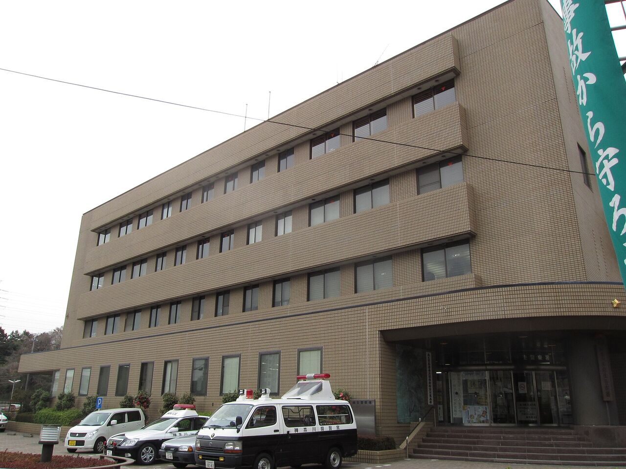 麻生警察署の建物。茶色いタイル張りの建物で、手前に警察の車などがとまっている