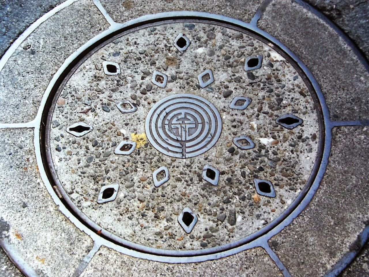 丸い下水のマンホールのふた。中央に川崎市の市章があり、まわりに穴が並ぶ