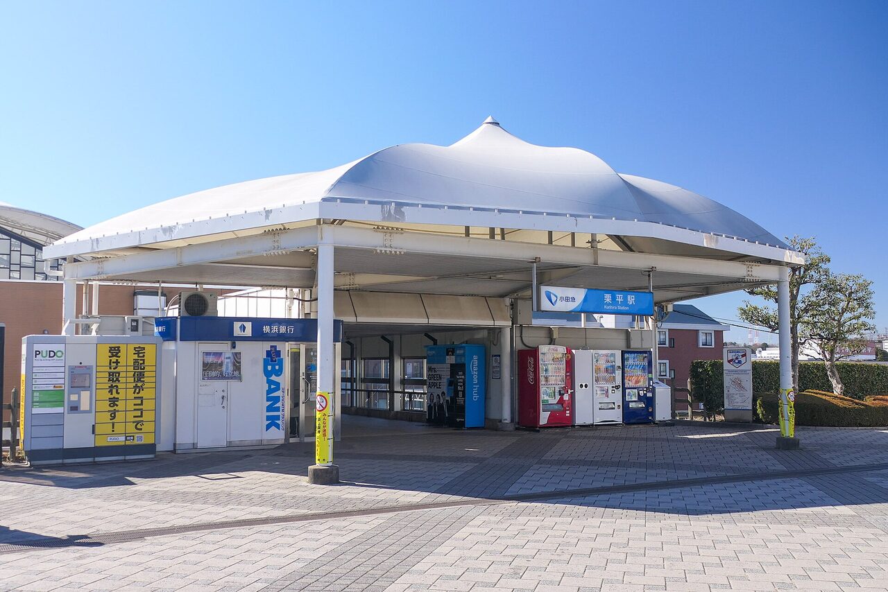 栗平駅の北口。白い屋根の下に、駅名の看板と宅配ロッカー、自動販売機が並んでいる