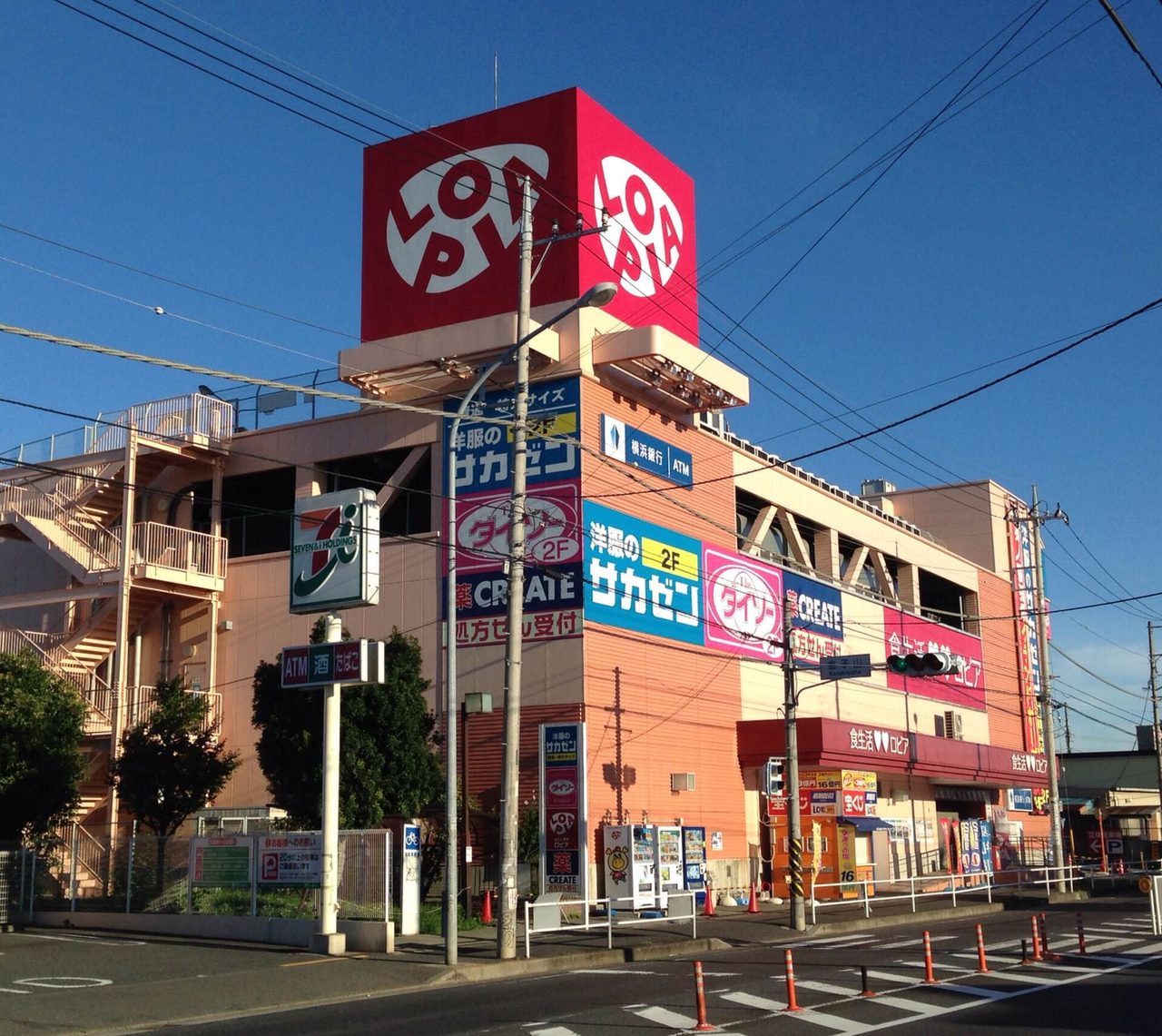 赤い四角の看板に「LOPIA」の文字がある建物。壁にほかの店の看板も並び、手前に交差点がある