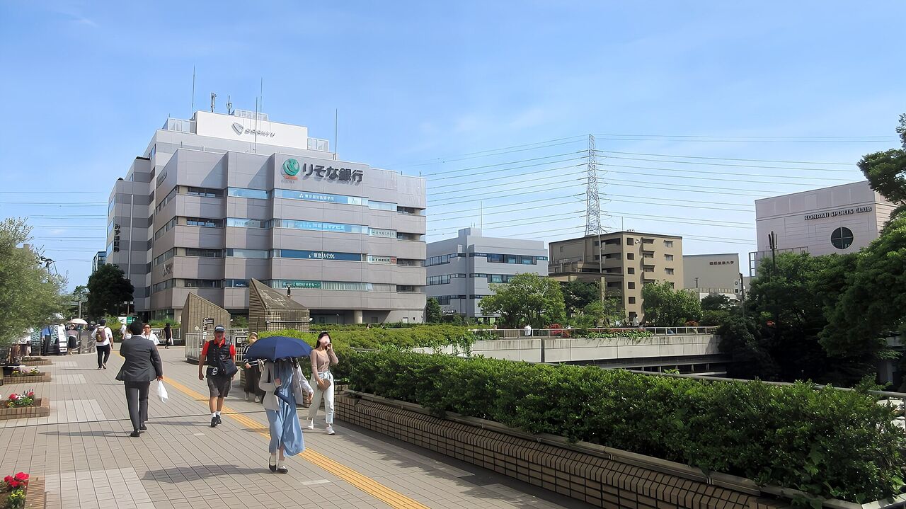 新百合ヶ丘駅前のペデストリアンデッキ。広い歩道橋の両側に木が並び、奥に駅前の建物が見える
