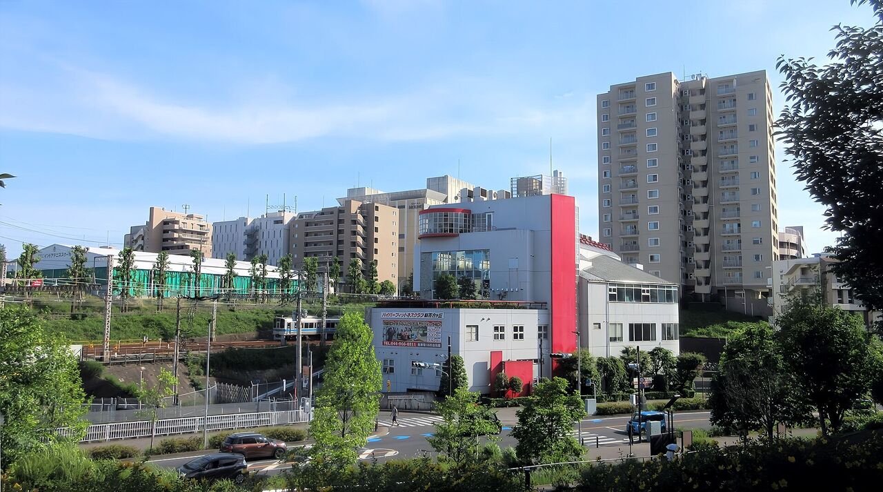 万福寺おやしろ公園から新百合ヶ丘駅の方向を見た景色。手前に木と道路、奥に線路と集合住宅が並ぶ