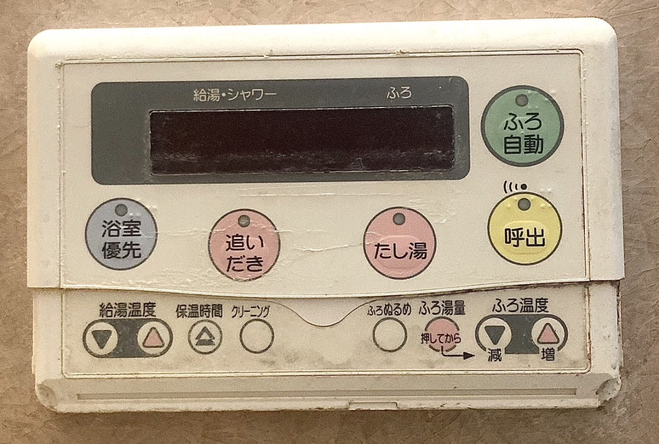浴室の壁にある古い給湯器のリモコン。「ふろ自動」「追いだき」「たし湯」「呼出」などの丸いボタンが並ぶ
