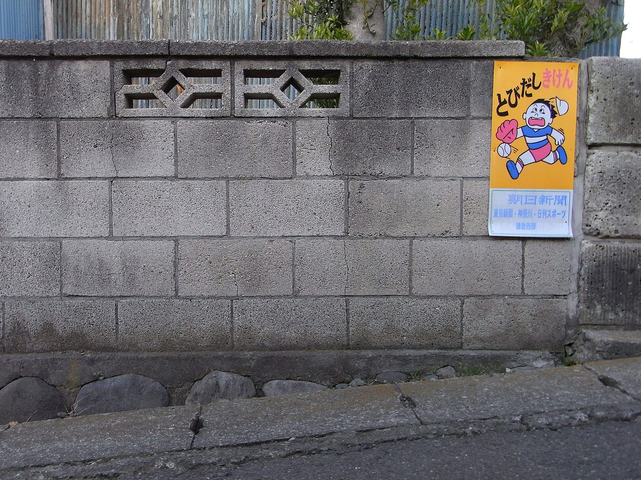 道路に面したコンクリートブロックの塀。上の段に飾りの穴あきブロックがあり、塀には飛び出し注意の看板が付いている（麻生区で撮った写真ではありません）