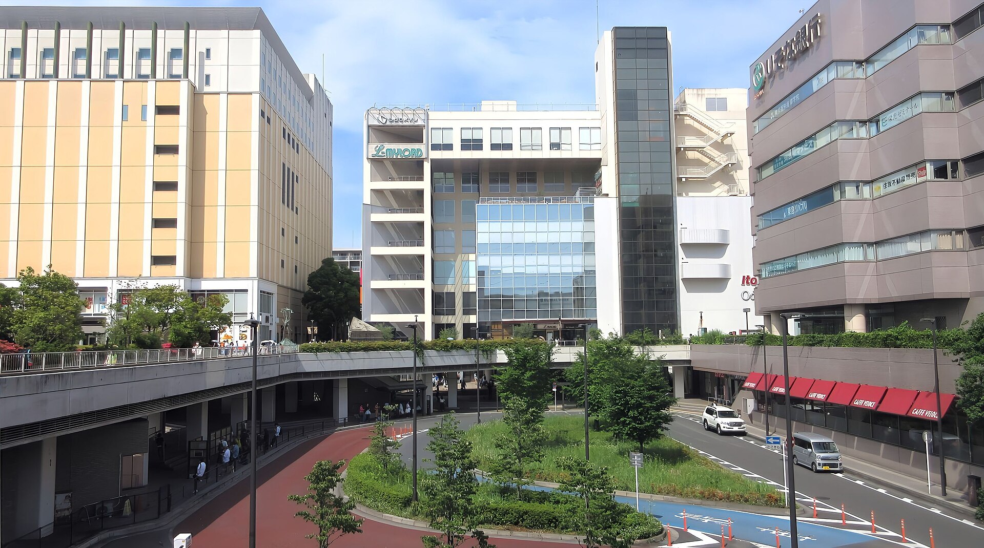 新百合ヶ丘駅南口のロータリー。正面に駅ビルの建物が並び、手前に緑の植え込みと道路が見える