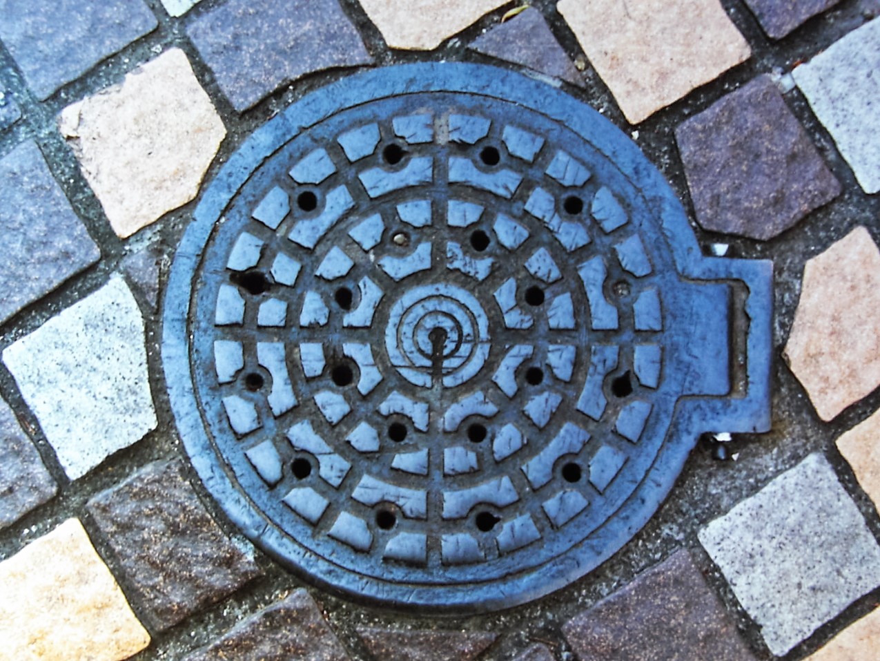 石畳の歩道にはめこまれた、丸い鉄のふた。小さな穴が輪の形に並んでいる