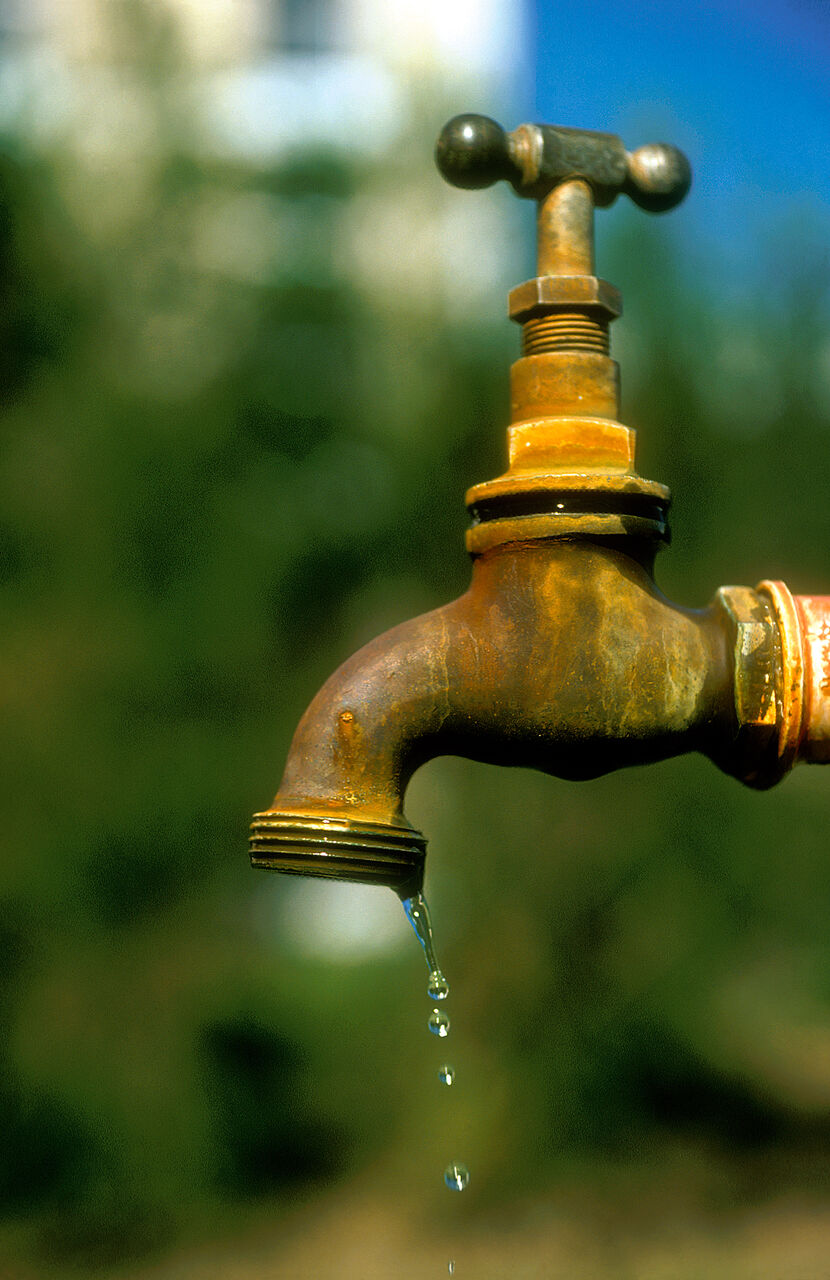 古い真ちゅうの蛇口。ハンドルが1つで、吐水口から水のしずくが落ちている