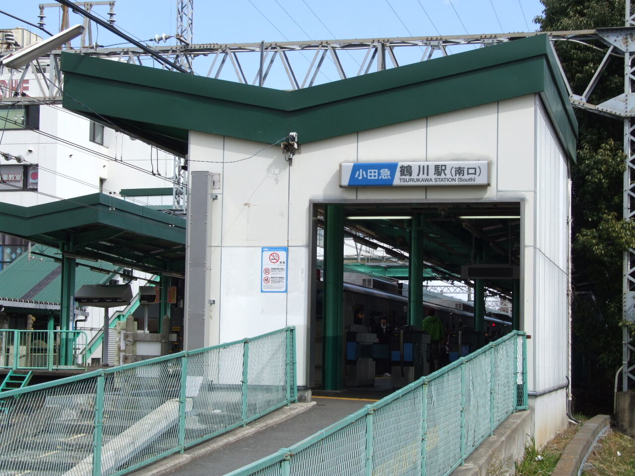 鶴川駅の南口。緑の屋根の駅舎に「鶴川駅（南口）」の看板があり、奥に改札と電車が見える