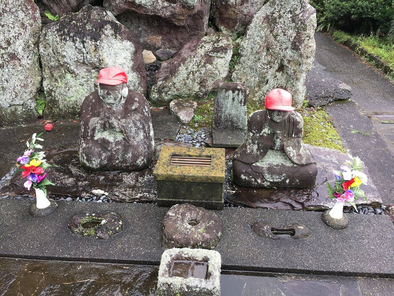 細山の道祖神。赤い帽子をかぶった2体の石の像の前に、花が供えられている